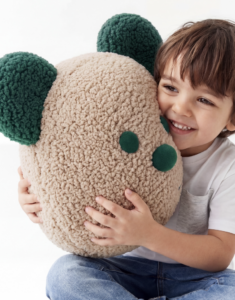 Smiling child hugging a large beige plush toy with green ears and nose
